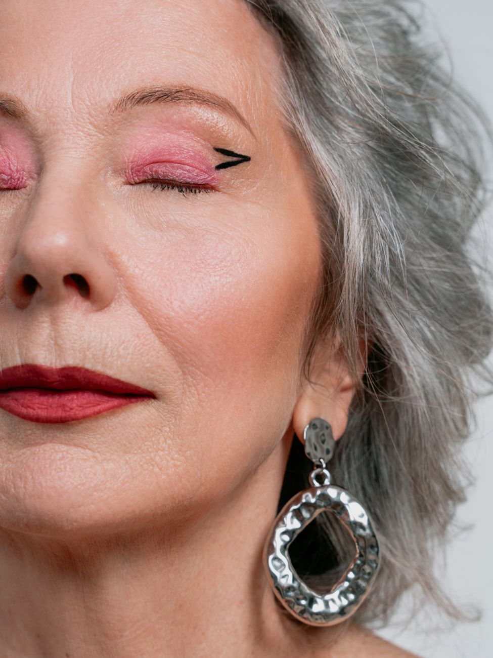 Silver-haired woman with pink eyeshadow and a large silver earring