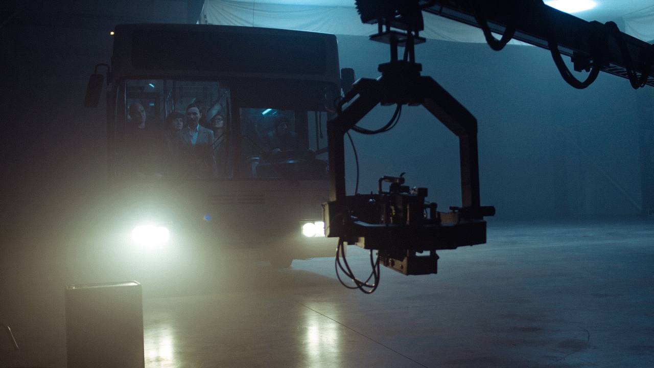 Camera on a crane arm in front of a bus full of actors in haze