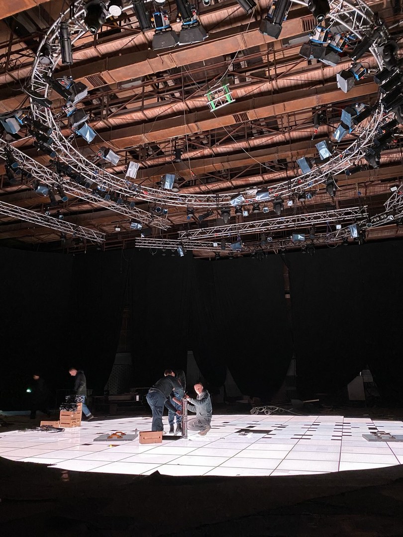 Lighting crew building a round LED stage under a ring of moving lights in a huge pavilion