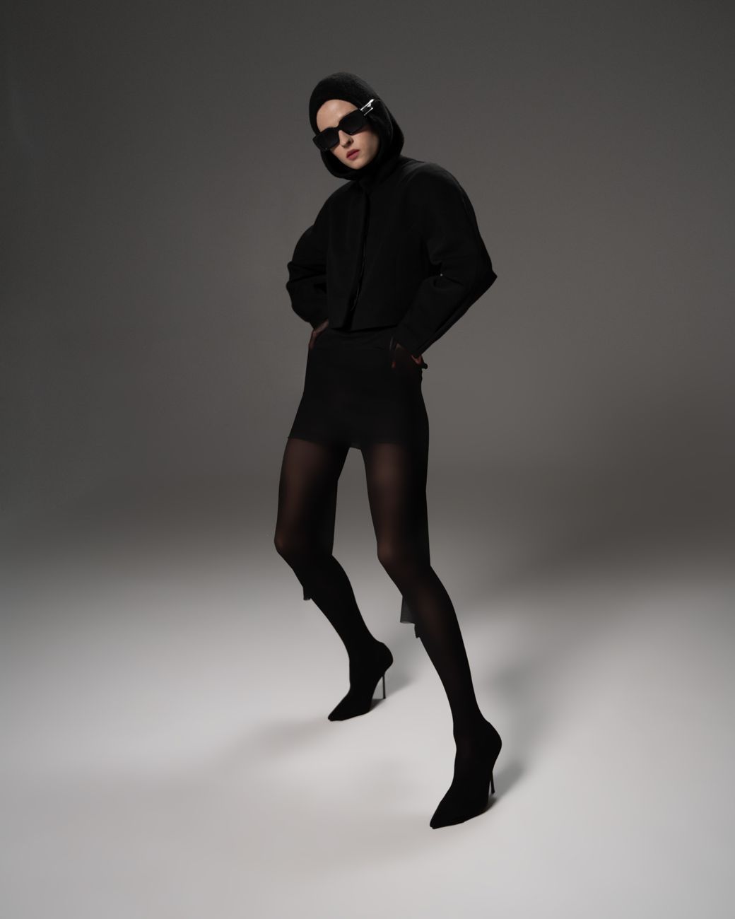 Model in an all-black look and sunglasses in studio light