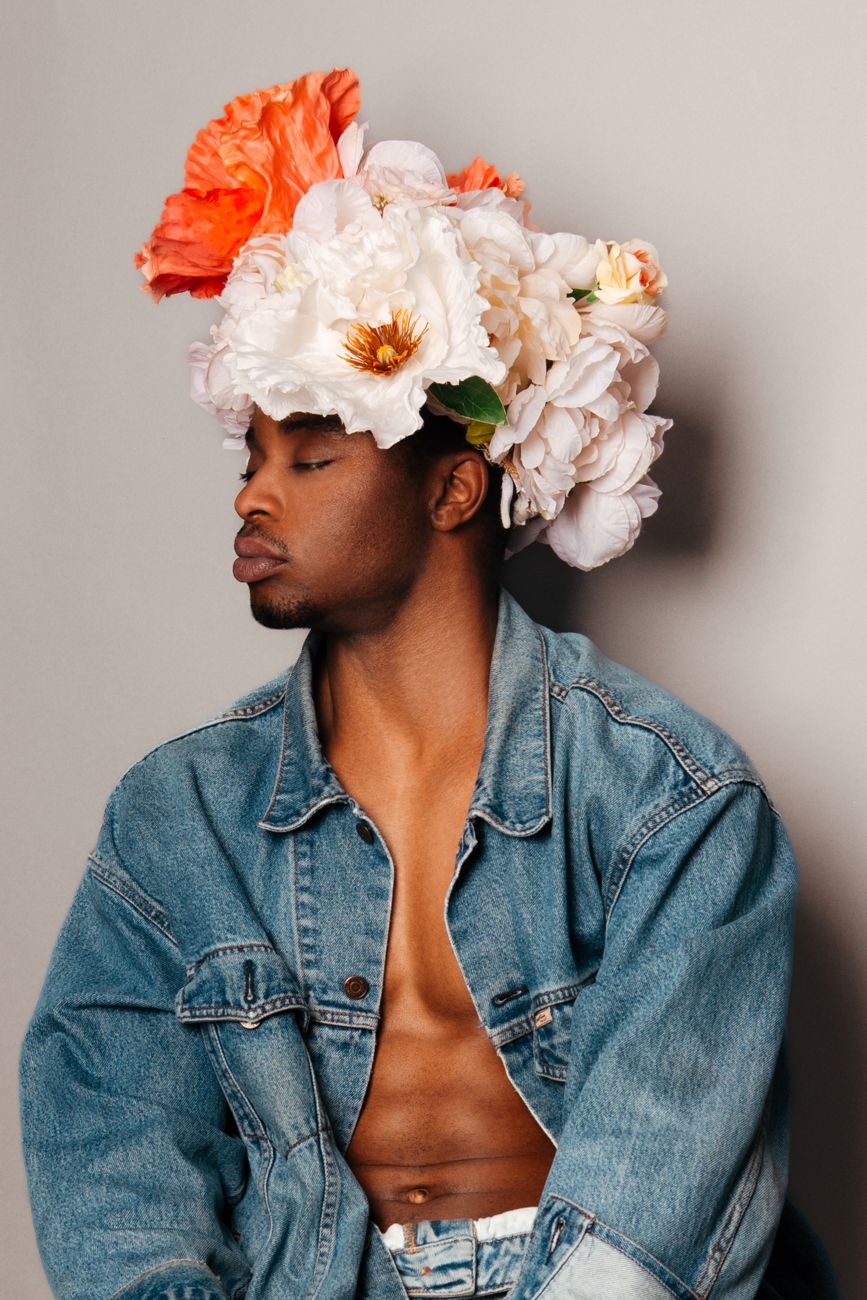Man in a denim jacket wearing a headpiece of white and orange flowers