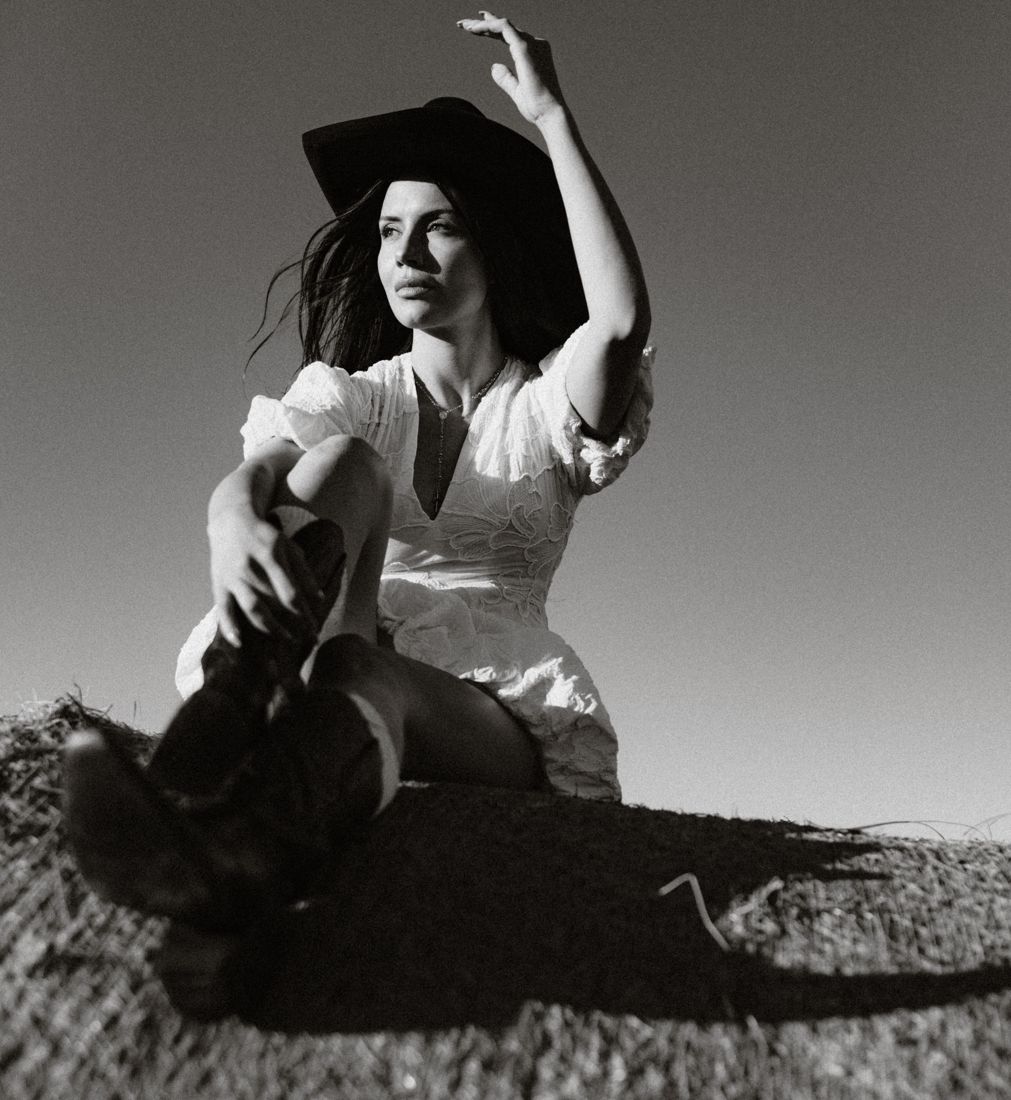 Black and white shot in a cowboy hat, arm raised, on a hay bale