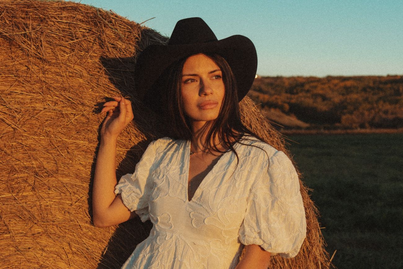 Golden-hour close-up in a black cowboy hat against a hay bale