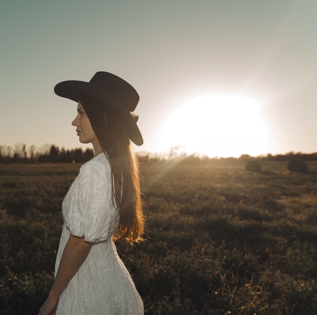 Profile in a cowboy hat with the sun setting over the field